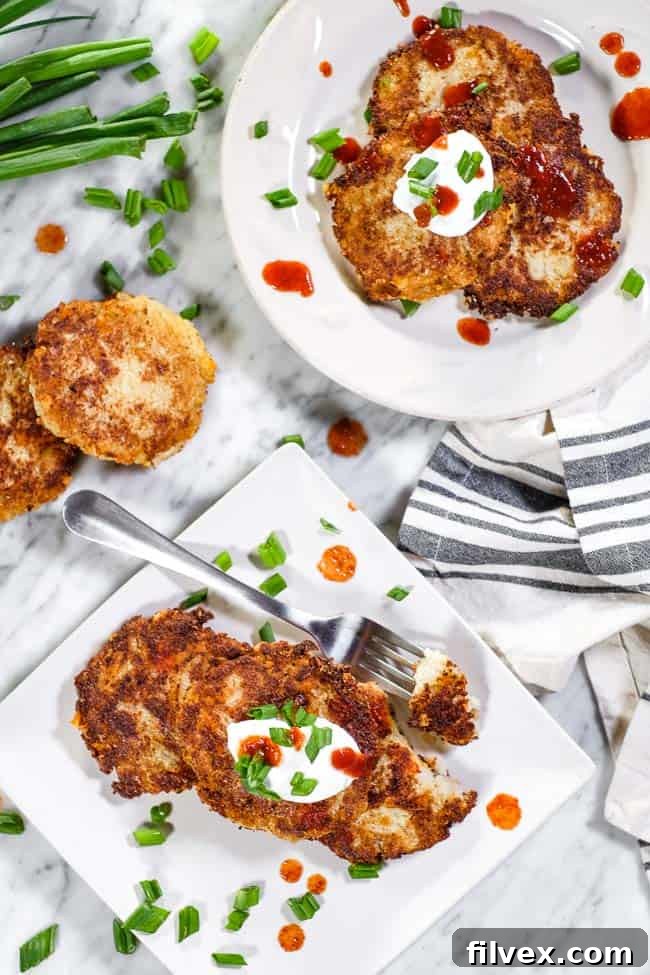 Cauliflower fritters laid on on two plates, topped with hot sauce, coconut yogurt and chopped green onion. One pate has a bite taken out on a fork.