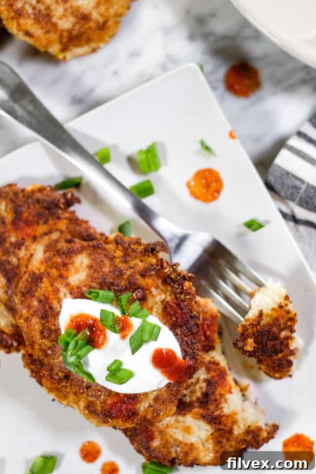 Close up of cauliflower fritters on a plate with a bit taken out on a fork. Topped with hot sauce, coconut yogurt and chopped green onion.