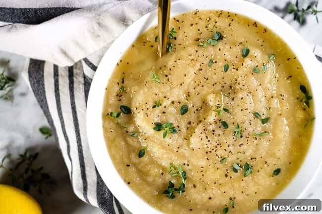 A bowl of creamy celeriac soup garnished with fresh thyme and ground black pepper, evoking comfort and warmth.
