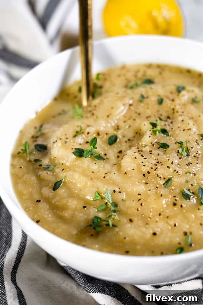 An angled view of creamy celeriac soup in a rustic bowl, garnished with fresh thyme and a sprinkle of black pepper, highlighting its comforting texture and aromatic appeal.
