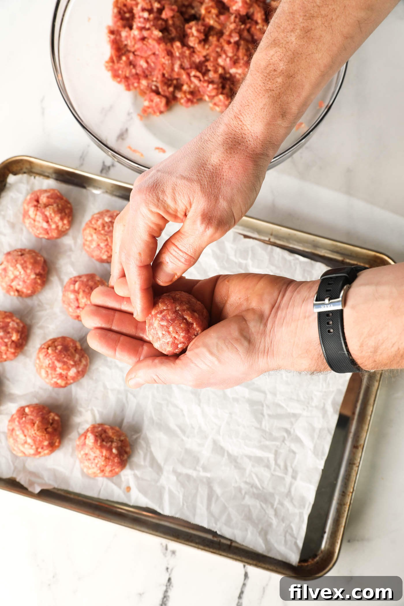 Hands forming ground pork into uniform meatballs