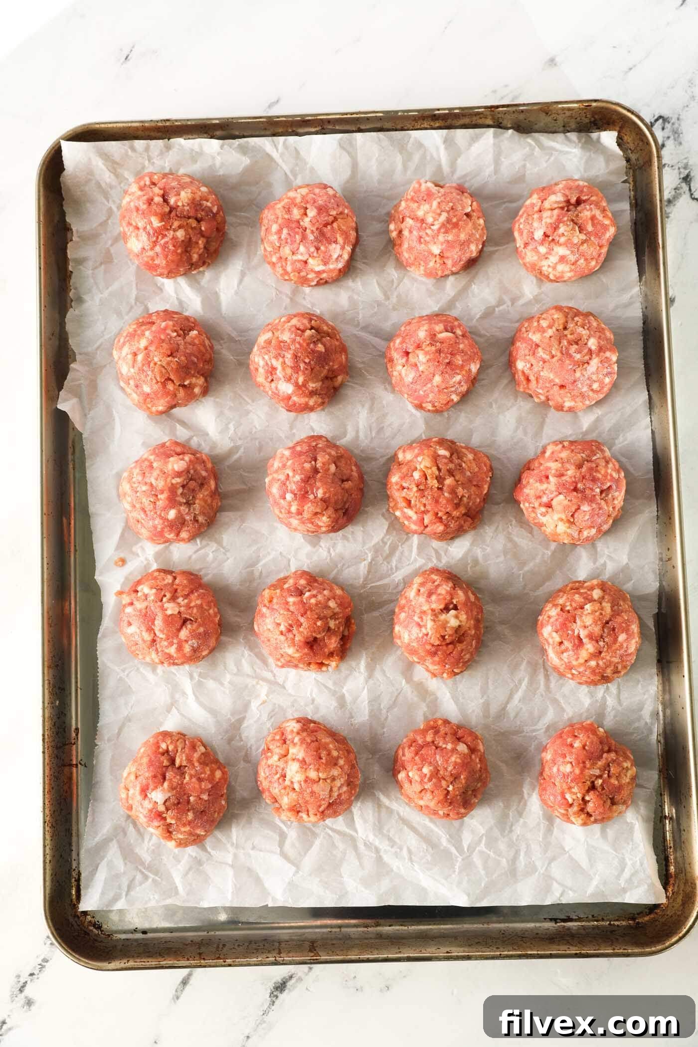 Baked pork meatballs on a parchment-lined baking sheet