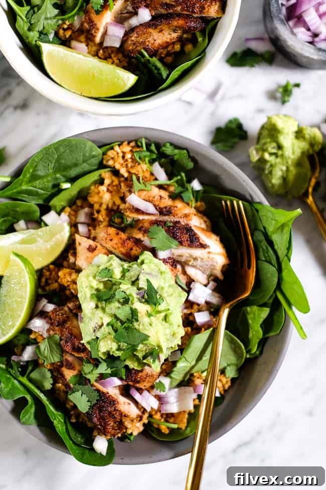 A close-up of a chicken burrito bowl, featuring tender chicken, fresh cilantro, creamy guacamole, diced red onion, and bright lime wedges, with a fork poised for a delicious bite.