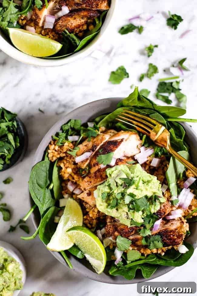 A close-up of a perfectly portioned chicken burrito bowl, garnished with fresh cilantro, diced red onion, creamy guacamole, and vibrant lime wedges, ready to be enjoyed with a fork.