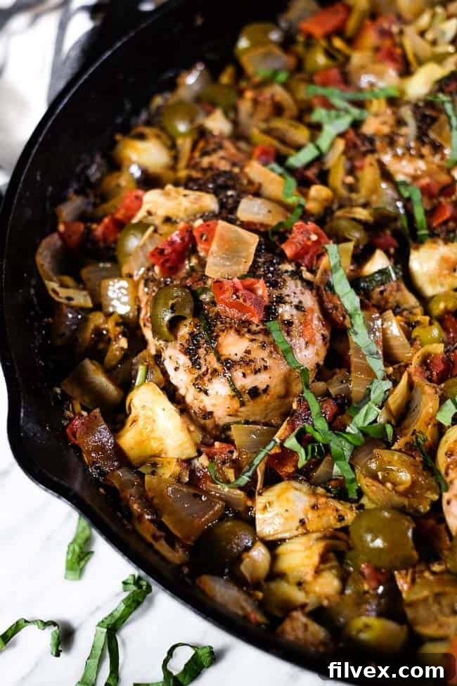 Close-up of succulent chicken pieces simmering in a rich, creamy tomato sauce within a large skillet, topped with fresh basil, ready to be served. 