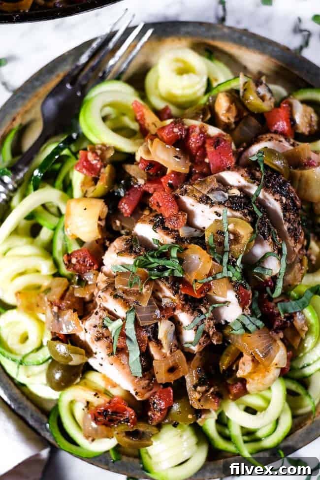 A close-up view of the perfectly cooked chicken in rich tomato sauce, served with fresh zoodles and garnished with basil, highlighting the appetizing texture and vibrant colors of the dish. 