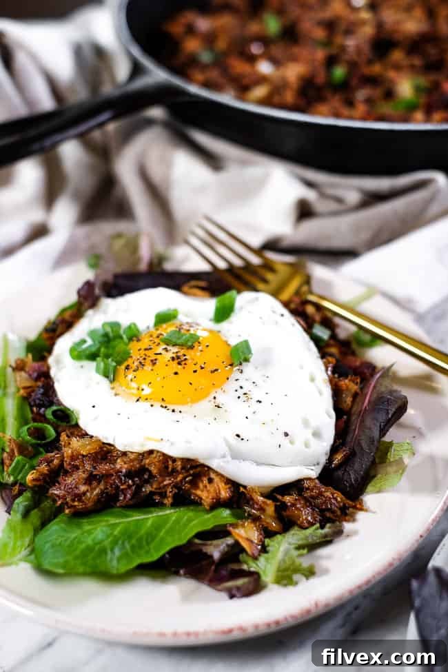A delicious portion of Leftover Pulled Pork Hash on a white plate, topped with a perfectly fried egg, ready for a gourmet breakfast.