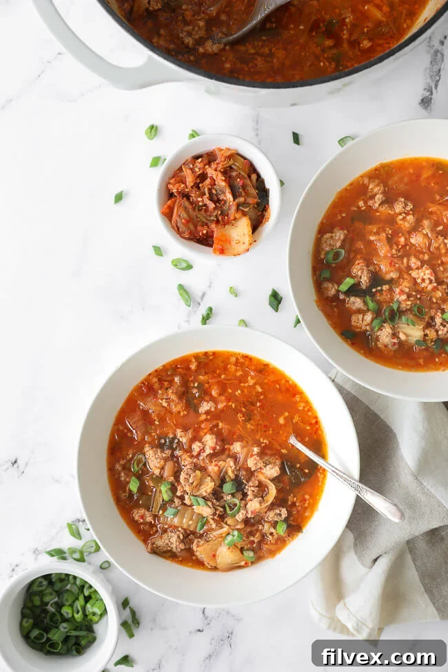 Overhead image of kimchi soup in soup pot and served up in two bowls with spoons in the bowls. 
