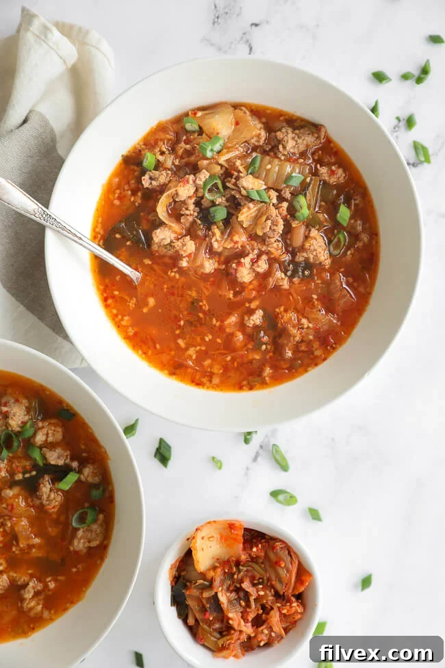 Overhead image of kimchi soup in a bowl with chopped green onion on top and a spoon dug into the bowl. 