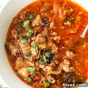 Close up overhead image of a bowl of delicious 25-minute Keto Kimchi Soup, garnished with fresh green onions and a spoon.