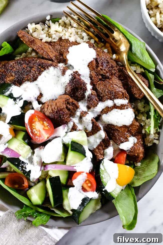 Close-up of a delicious Beef Shawarma Bowl, featuring tender seasoned beef, fresh greens, cauliflower rice, and vibrant vegetables, drizzled with dairy-free tzatziki.