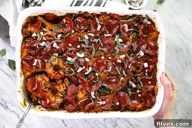 Overhead shot of spaghetti pizza casserole in casserole dish with serving spoon in one corner and holding the dish with one hand. 