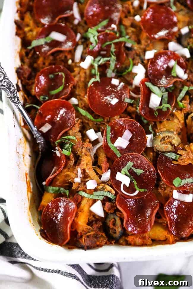 Close up overhead shot of spaghetti pizza casserole in casserole dish. Topped with fresh chopped red onion and basil. 