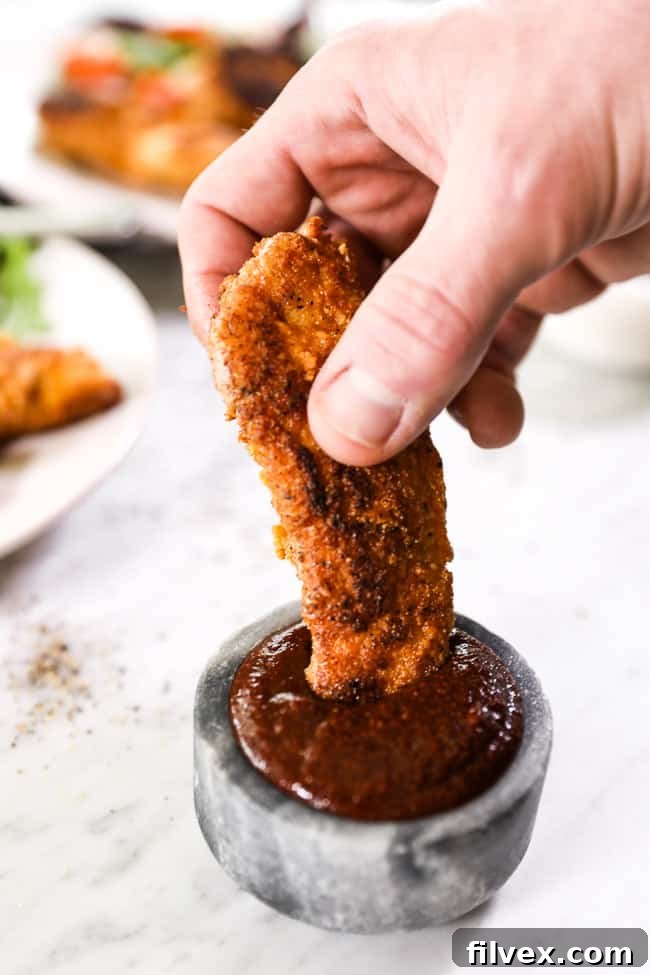 A piece of paleo fried chicken being dipped into ramekin of BBQ sauce. 