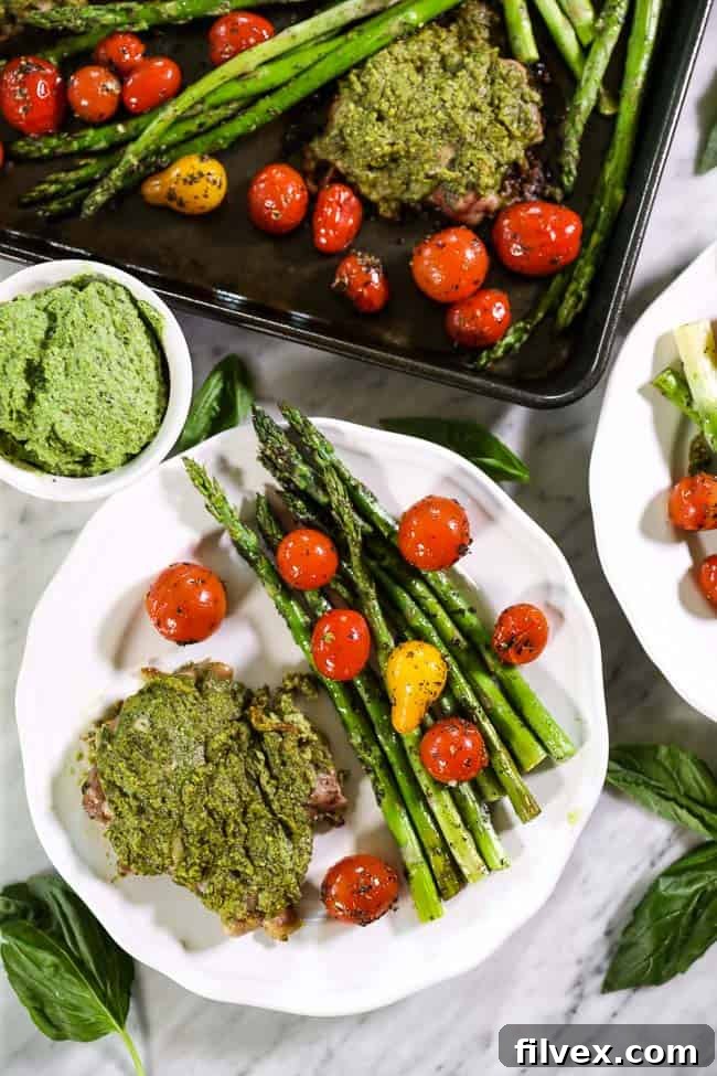 Easy baked pesto chicken on single plate with tomatoes and asparagus sheet pan on top of image