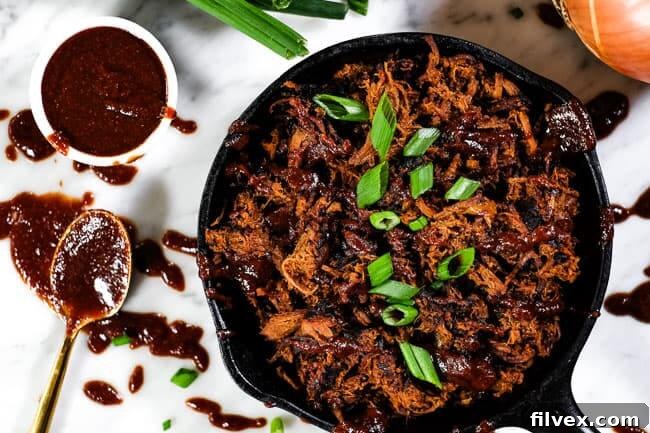 Slow cooker BBQ beef served in a cast iron skillet, garnished with extra BBQ sauce and chopped green onions. A messy spoon rests beside a small dish of additional sauce.