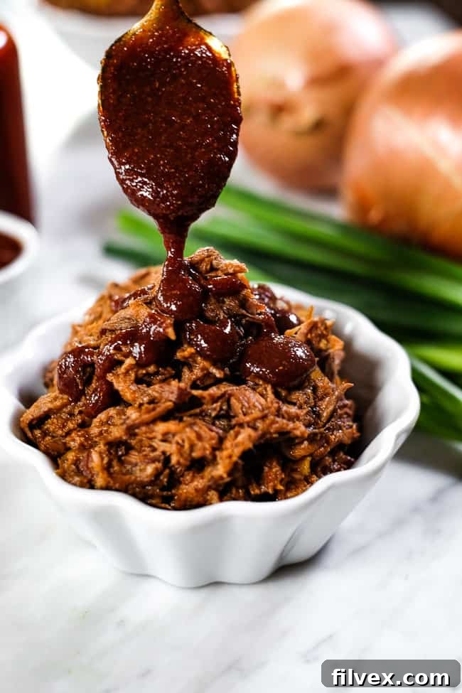 A close-up shot of BBQ sauce being drizzled over slow cooker BBQ beef in a ramekin, with chopped green onions in the background.