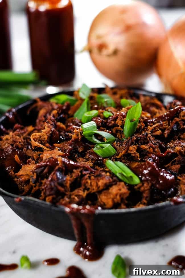 An overhead angled view of slow cooker BBQ beef presented in a cast iron skillet, generously topped with additional BBQ sauce and freshly chopped green onions.