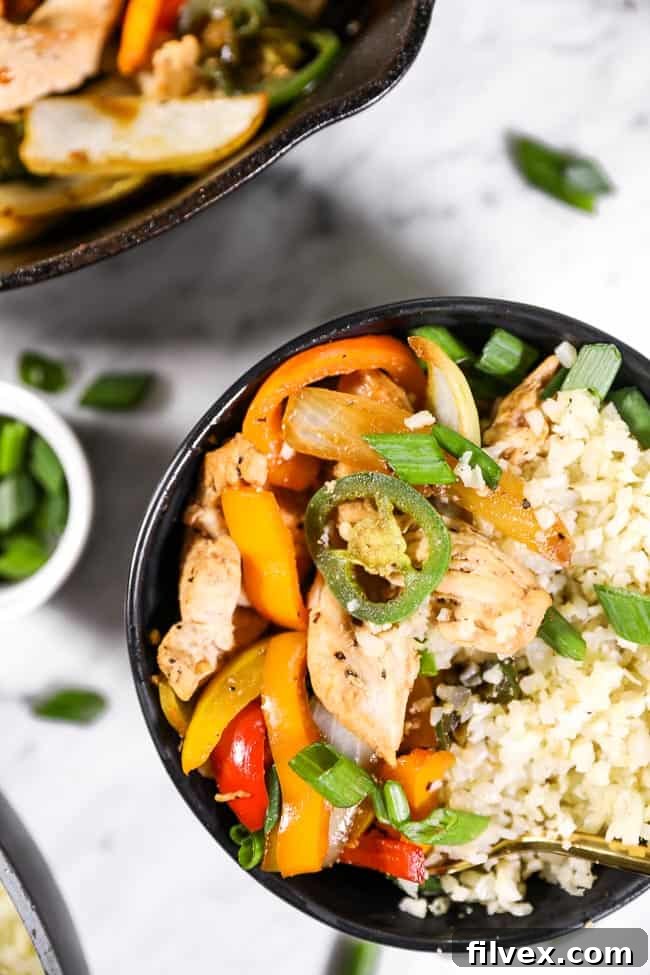 Thai basil chicken served in a bowl with cauliflower rice and topped with chopped green onion. 