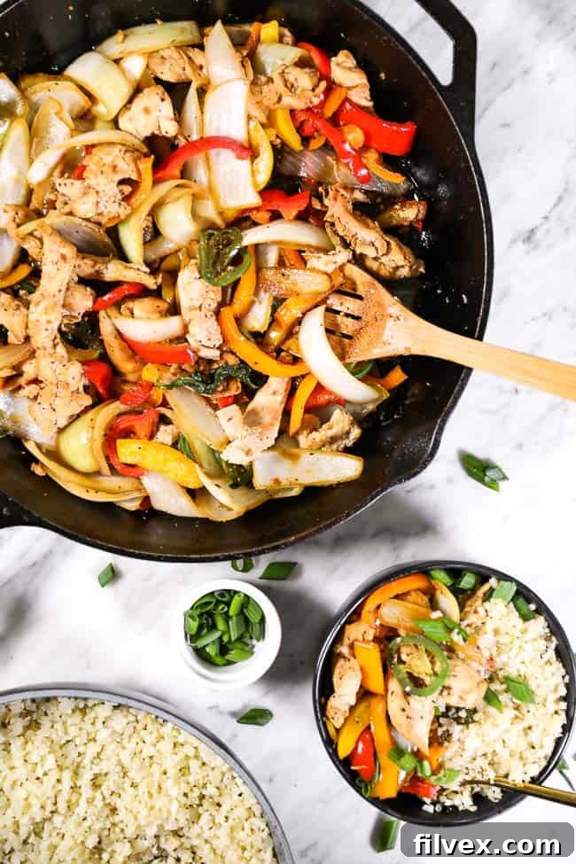Thai basil chicken in a cast iron skillet and served up in a bowl with cauliflower rice. Topped with chopped green onion. 