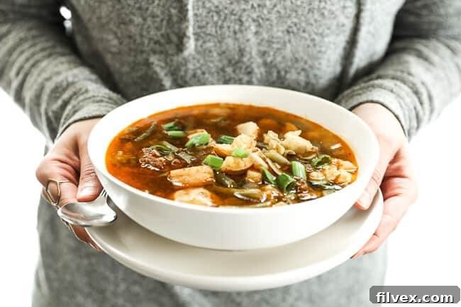 A person holding a bowl of hearty Paleo and Whole30 Hamburger Soup, showcasing its rich texture and steam, ready to be enjoyed.