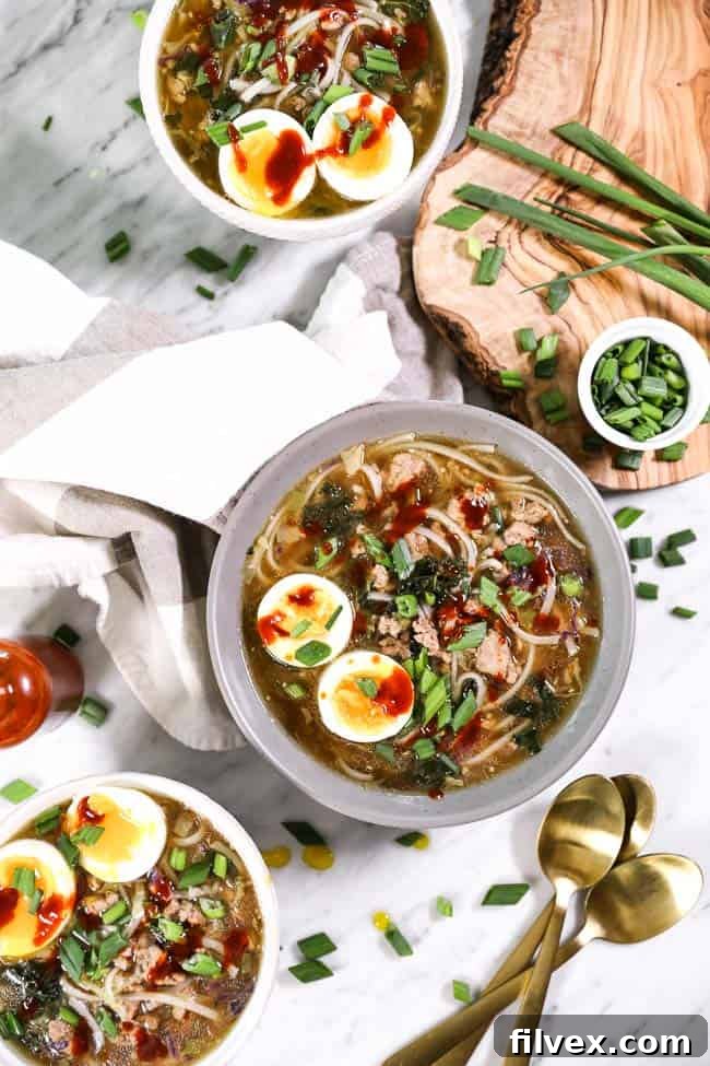 Three bowls of pork ramen noodles, topped with chopped green onion, soft boiled eggs and hot sauce. 