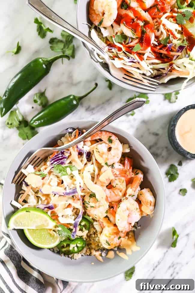 Two beautifully plated cilantro lime shrimp bowls, each featuring succulent shrimp, cauliflower rice, fresh toppings, and a generous drizzle of sauce. Forks are resting in the bowls, inviting viewers to savor this healthy and easy weeknight dinner.