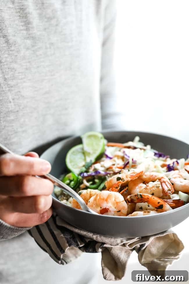 A person digging a fork into a cilantro lime shrimp bowl, featuring a close-up of the fresh ingredients like shrimp, avocado, and jalapeño, all coated in a delicious sauce. This image conveys the enticing and ready-to-eat nature of the healthy meal.