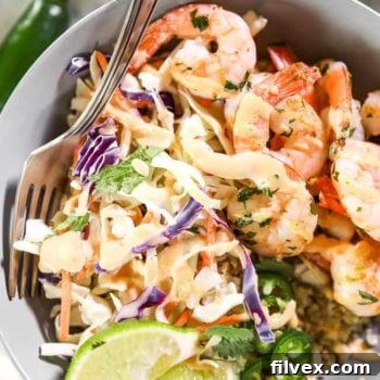 Close up shot of cilantro lime shrimp bowl with fork in it, topped with sauce, jalapeño slices and lime wedges.