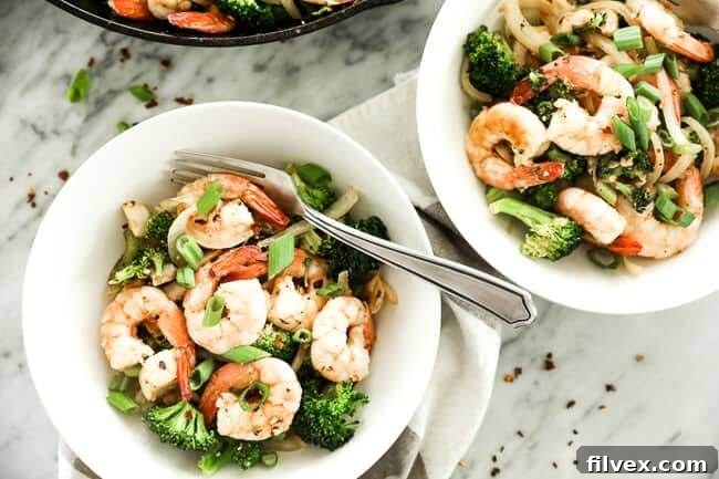 Two bowls of vibrant Paleo and Whole30 seafood stir-fry, featuring succulent shrimp, flaky white fish, crisp broccoli florets, thinly sliced celery, and sweet onion, all seasoned with a rich Cajun blend and garnished with fresh green onions and a sprinkle of red pepper flakes.
