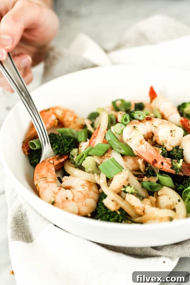 A single bowl showcasing a generous serving of Paleo and Whole30 seafood stir-fry, featuring plump shrimp, succulent white fish, crisp broccoli, tender celery, and sweet onion, all glistening with a savory Cajun seasoning. A fork is poised within the bowl, adorned with fresh green onion and red pepper flakes, ready to be enjoyed.