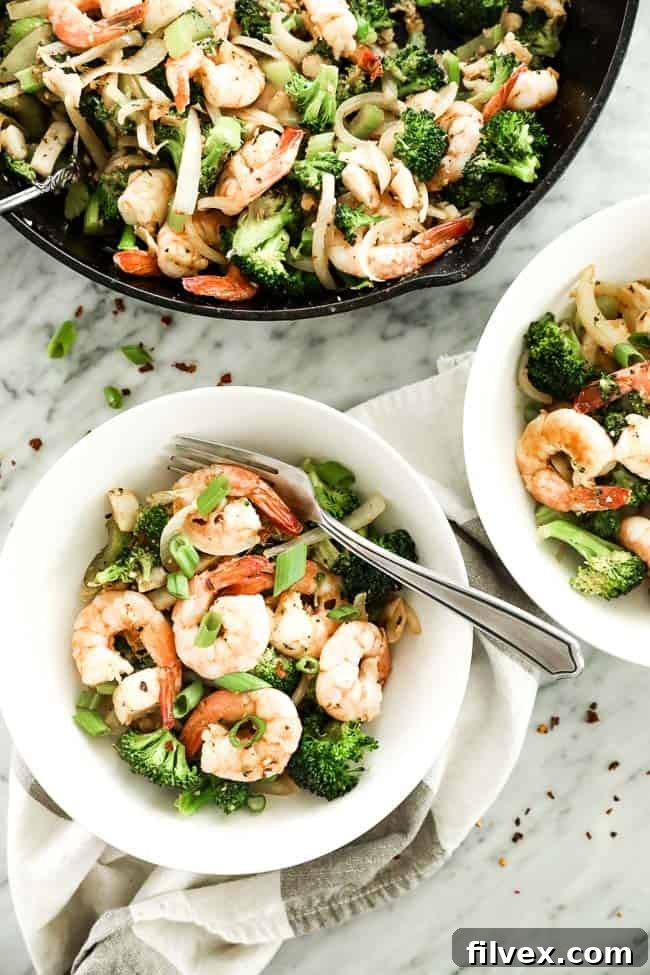 An appetizing display of Paleo and Whole30 seafood stir-fry, presented in two serving bowls and a cast iron skillet. The stir-fry is rich with shrimp, white fish, bright green broccoli, crisp celery, and savory onion, all infused with a flavorful Cajun seasoning. Each serving is elegantly garnished with chopped green onions and a sprinkle of red pepper flakes, with a fork invitingly placed in one bowl.