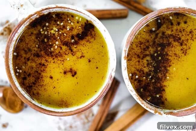 Two mugs of golden milk latte, topped with cinnamon and hemp seeds. The drink is a creamy, cozy, and satisfying caffeine-free turmeric latte, perfect for a complete morning. Also great as an afternoon or evening beverage due to being caffeine-free. It's Paleo, Whole30, Keto, and Vegan.