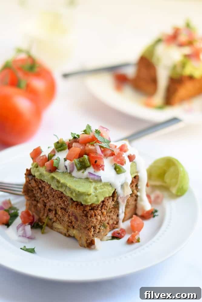 Layered taco casserole piece on plate with tomato topping