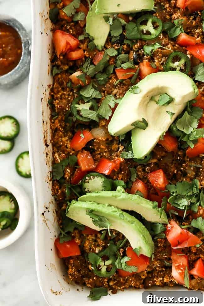 Image of easy taco casserole in white casserole dish, topped with chopped tomato, fresh cilantro, sliced jalapeño and avocado. 