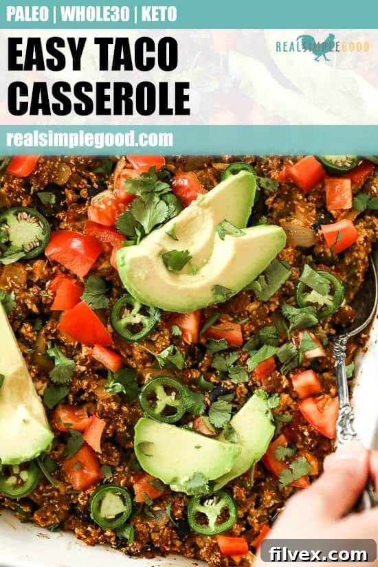 Image of easy taco casserole in white casserole dish with serving spoon, topped with chopped tomato, fresh cilantro, sliced jalapeño and avocado. 