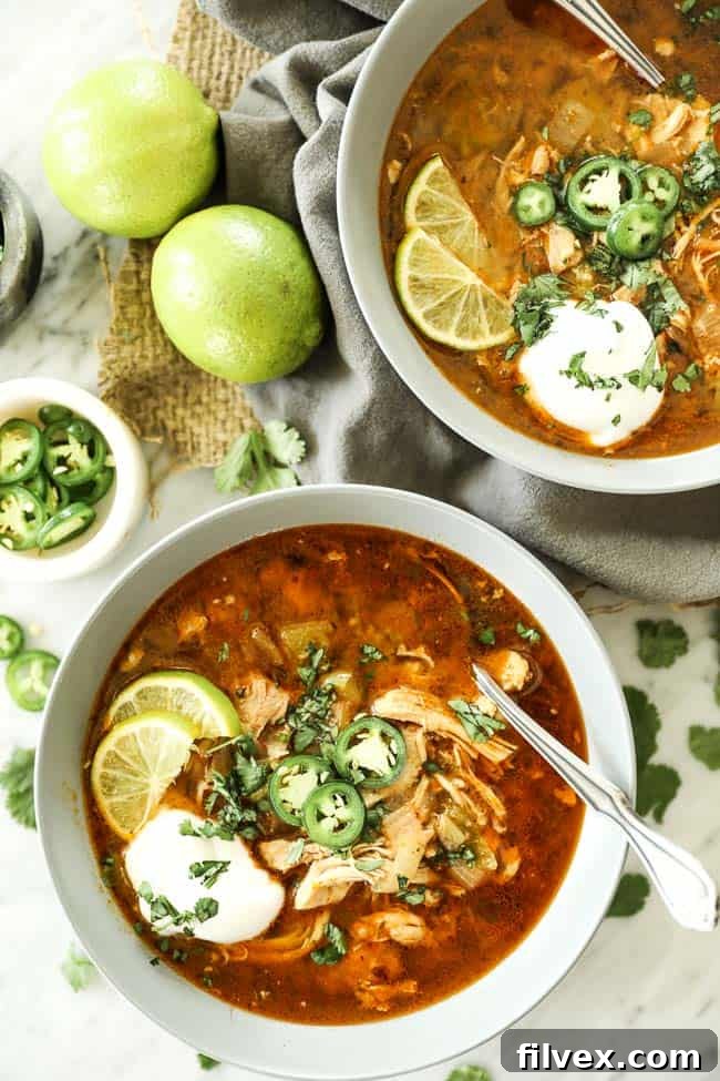 Instant Pot White Chicken Chili served in two bowls with various fresh toppings like cilantro and avocado. A hand is holding a spoon, ready to dig in.