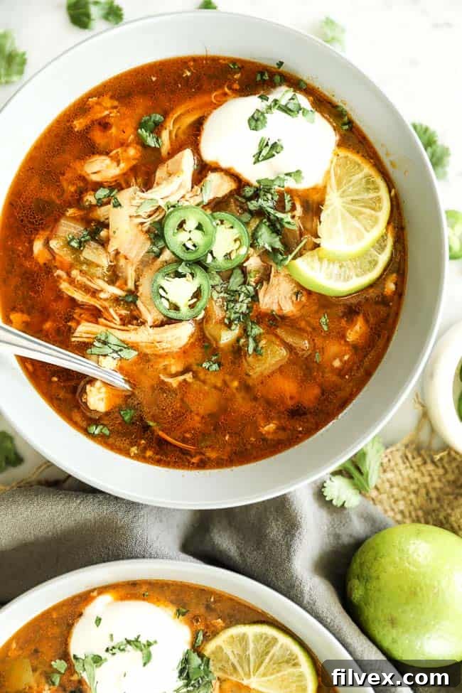 Close-up vertical shot of Instant Pot White Chicken Chili in a bowl, generously topped with fresh ingredients and a spoon.