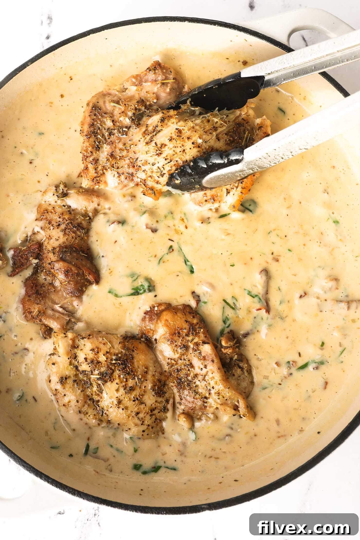 Cooked chicken being returned to the skillet with the creamy Tuscan sauce.