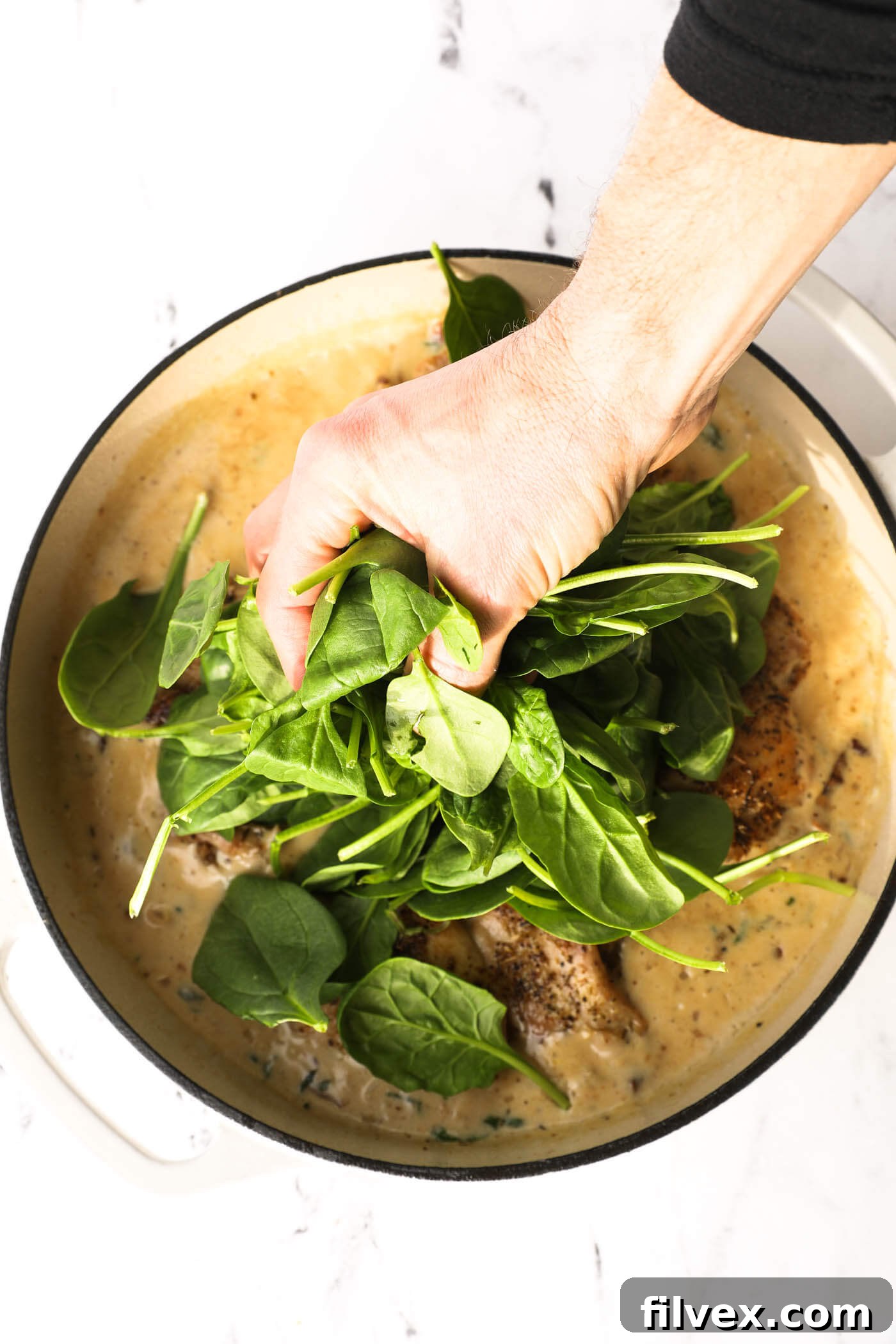 Fresh spinach being added to the creamy Tuscan chicken sauce in the skillet.