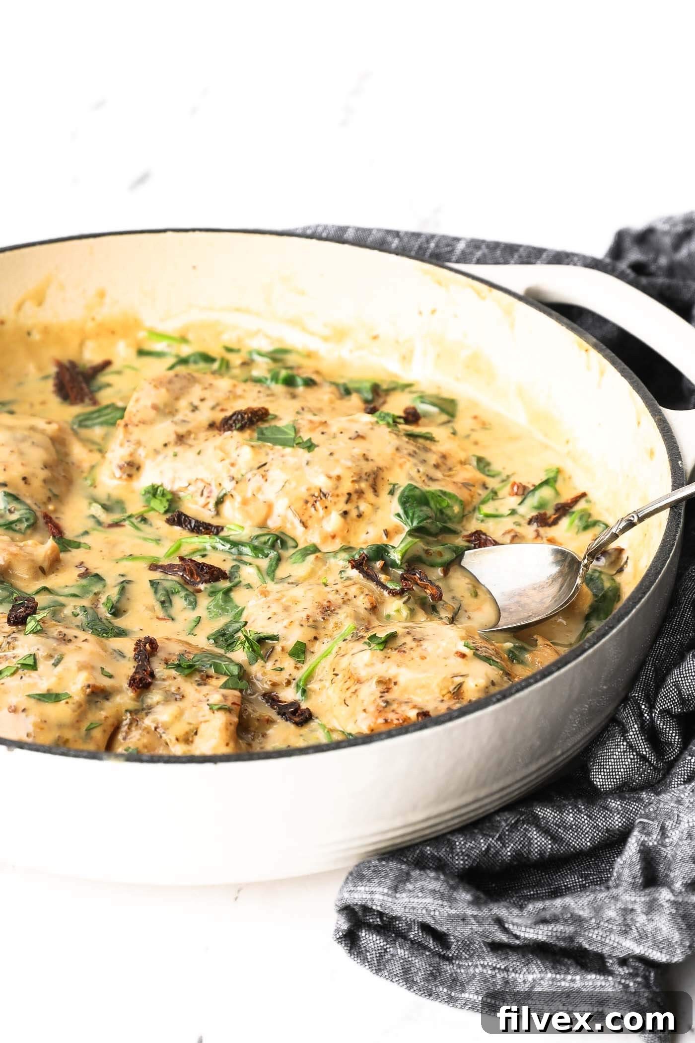 A close-up of a serving of creamy Tuscan chicken with a fork, showing the rich sauce and spinach.