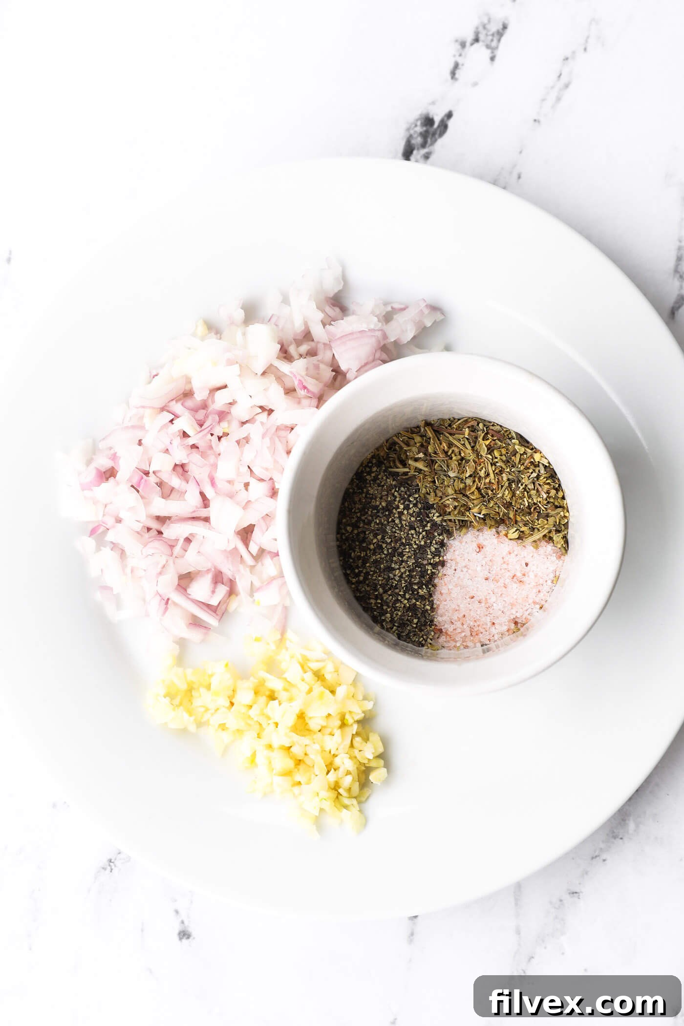 Close-up of diced shallot and minced garlic next to a bowl of Italian seasoning mix.