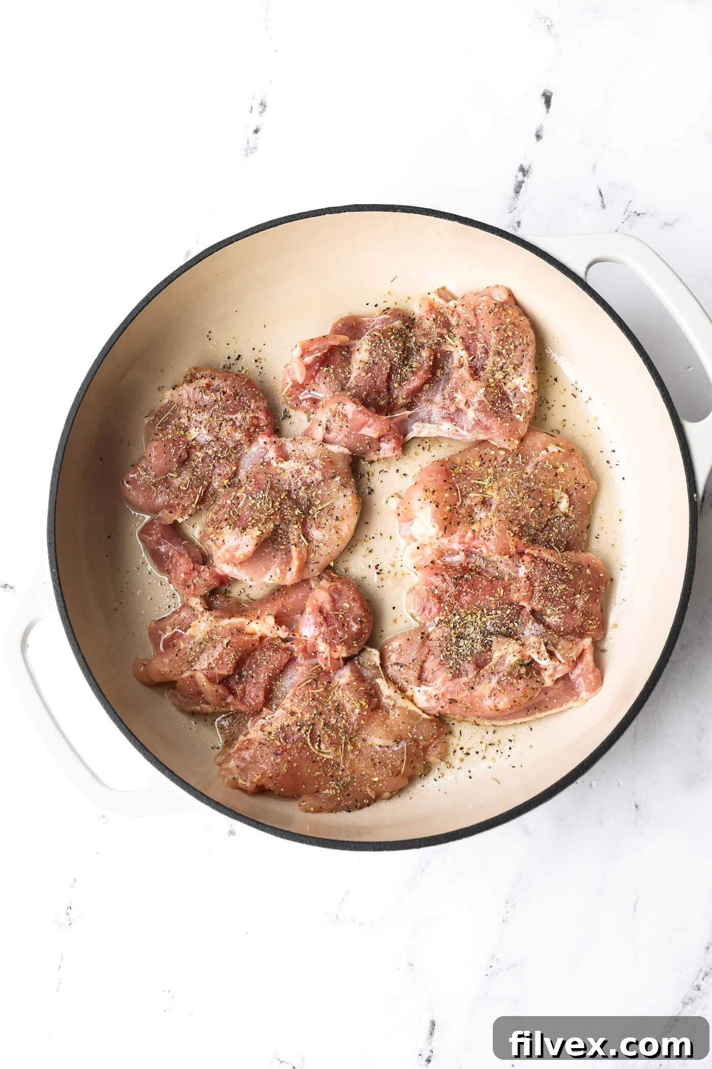 Chicken thighs searing in a hot skillet, developing a golden-brown crust.