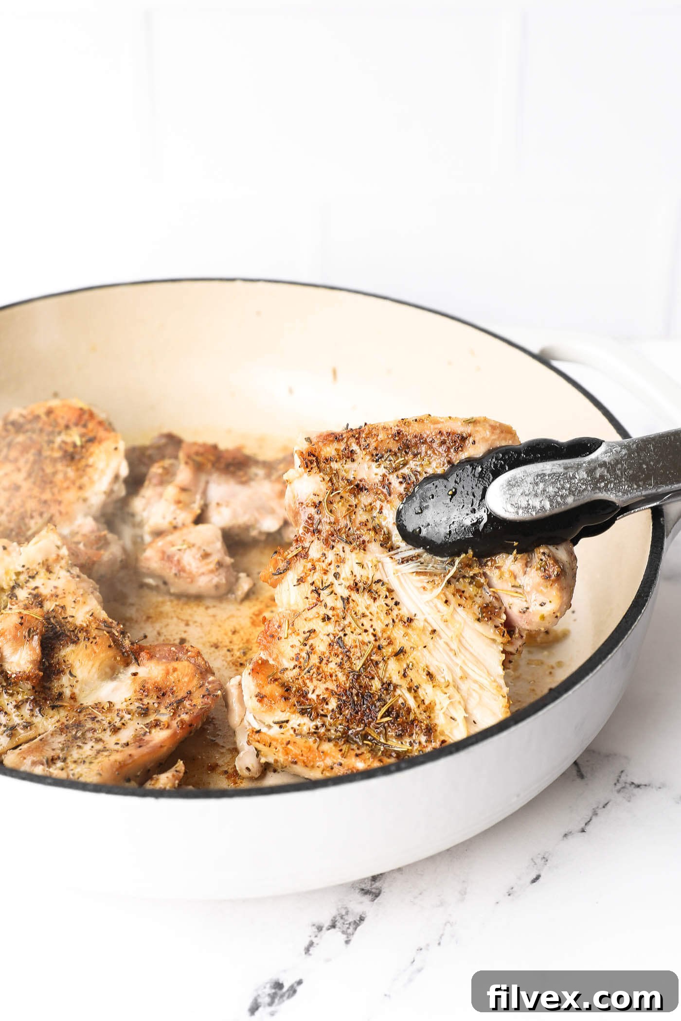 Cooked chicken being flipped in the skillet to brown the other side.