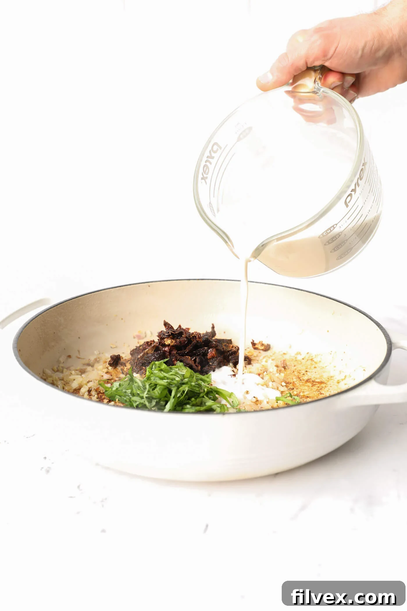 Sun-dried tomatoes and basil added to the sautéed aromatics in the skillet, with coconut milk being poured in.