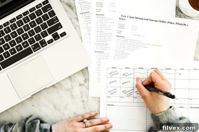 Hands filling out grocery list with computer on left side