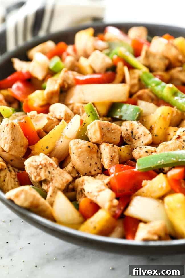 Angled shot of sweet and sour chicken in a skillet. Dish includes chicken, onion, red and green bell pepper, pineapple and a sweet and sour sauce. 