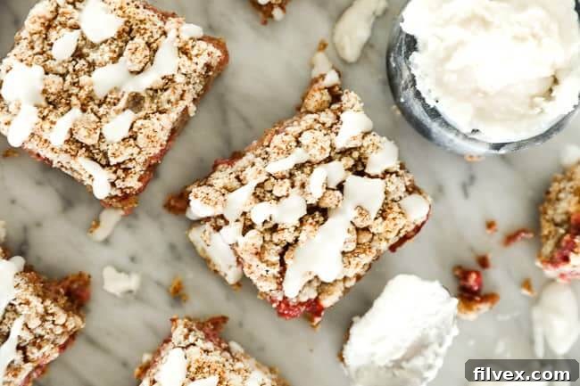 Close-up image of freshly baked strawberry crumble bars with a delicate coconut butter drizzle on top, artfully arranged on a pristine marble surface. A small, elegant dish holds extra coconut butter and a spoon, hinting at the delicious topping. The vibrant red of the strawberries peeks through the golden crumble, inviting a bite.