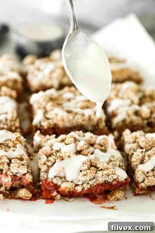 Image showcasing the elegant act of drizzling warm, smooth coconut butter generously over the top of freshly baked strawberry crumble bars. The white drizzle contrasts beautifully with the golden-brown crumble and the hints of red strawberry filling, creating an enticing visual.