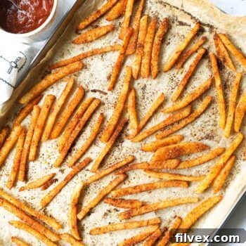 Seasoned crispy jicama fries on a sheet pan with ketchup on the side